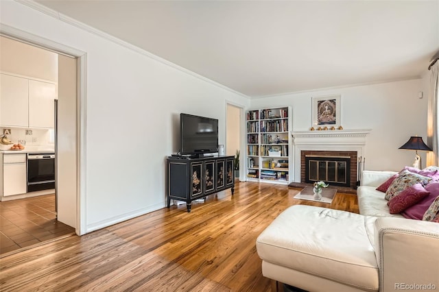 living room featuring ornamental molding, light wood-type flooring, a brick fireplace, and built in shelves