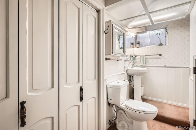 half bath with wainscoting, toilet, and wallpapered walls