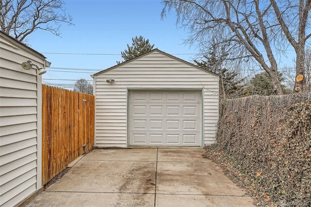 detached garage featuring concrete driveway and fence