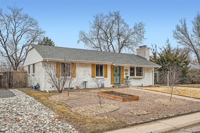 ranch-style home with roof with shingles, a chimney, fence, and brick siding