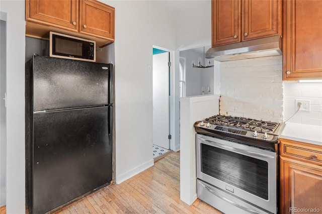 kitchen with gas range, light hardwood / wood-style flooring, decorative backsplash, and black refrigerator