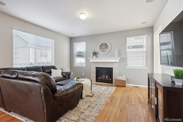 living room with light hardwood / wood-style floors, a wealth of natural light, and a tiled fireplace