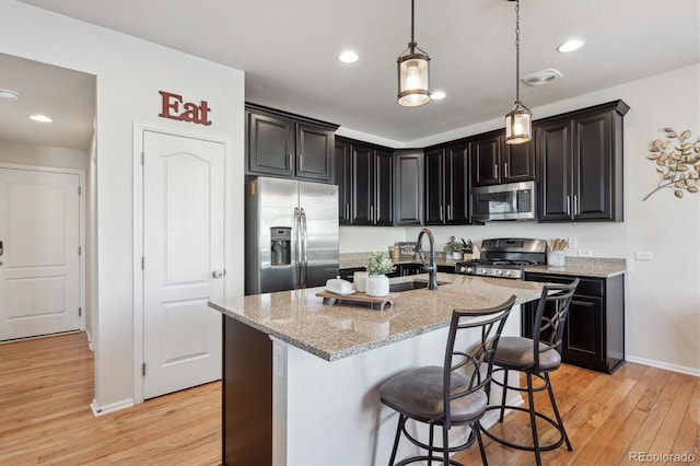 kitchen featuring a center island with sink, sink, a breakfast bar area, stainless steel appliances, and light stone counters