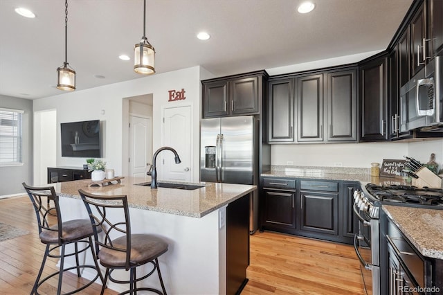 kitchen with pendant lighting, appliances with stainless steel finishes, sink, light stone counters, and a center island with sink