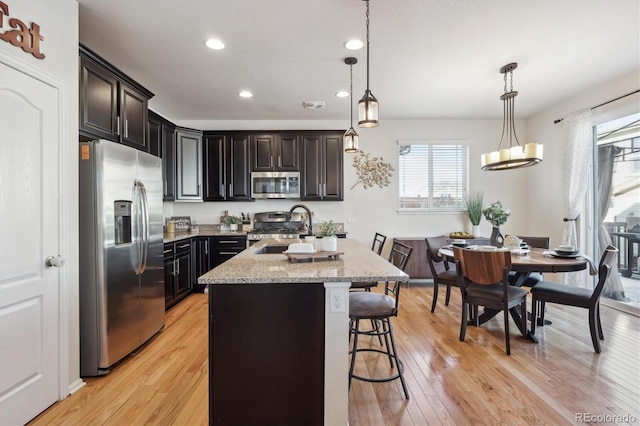 kitchen featuring decorative light fixtures, stainless steel appliances, sink, a center island with sink, and a breakfast bar area