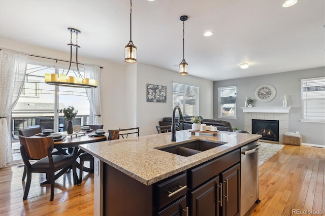 kitchen featuring dishwasher, decorative light fixtures, a fireplace, sink, and a kitchen island with sink