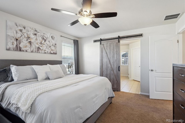 bedroom with ceiling fan, light colored carpet, and a barn door