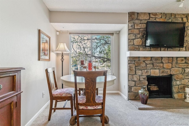 dining space featuring baseboards, a fireplace, a textured ceiling, and light colored carpet