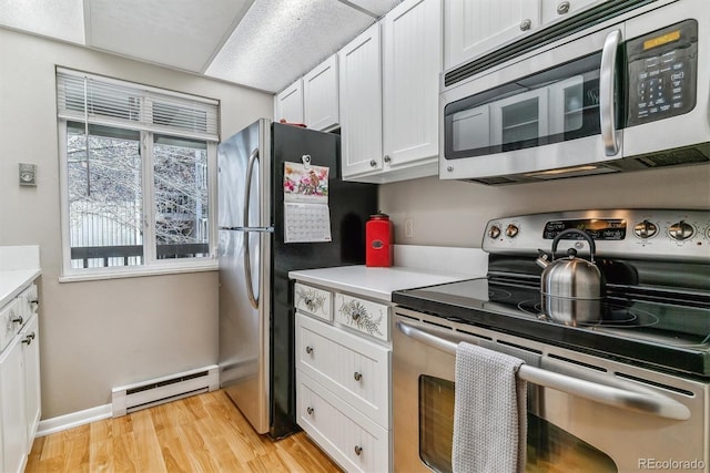 kitchen with appliances with stainless steel finishes, a baseboard radiator, light countertops, white cabinetry, and light wood-type flooring