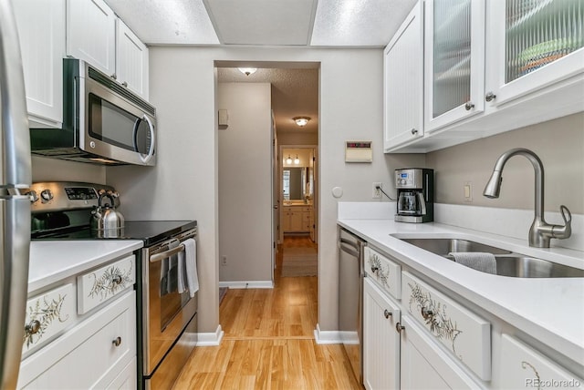 kitchen featuring light countertops, white cabinets, a sink, light wood finished floors, and appliances with stainless steel finishes