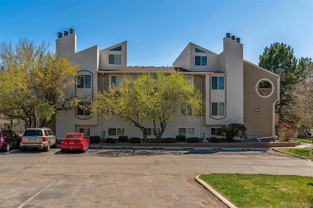 exterior space with a chimney, stucco siding, and uncovered parking