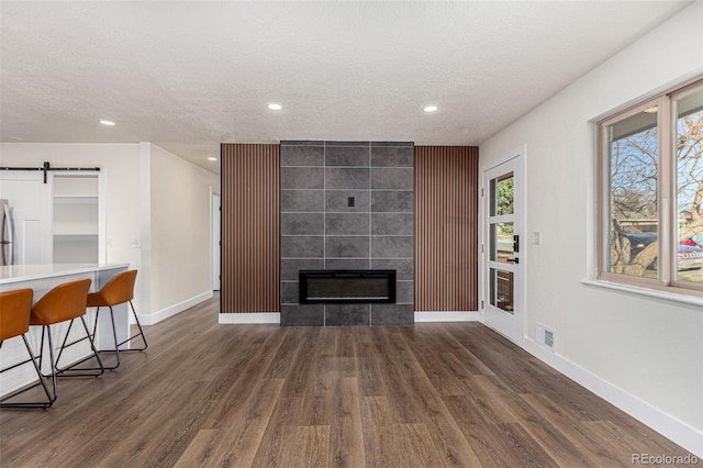 living area featuring visible vents, baseboards, a tiled fireplace, a barn door, and wood finished floors