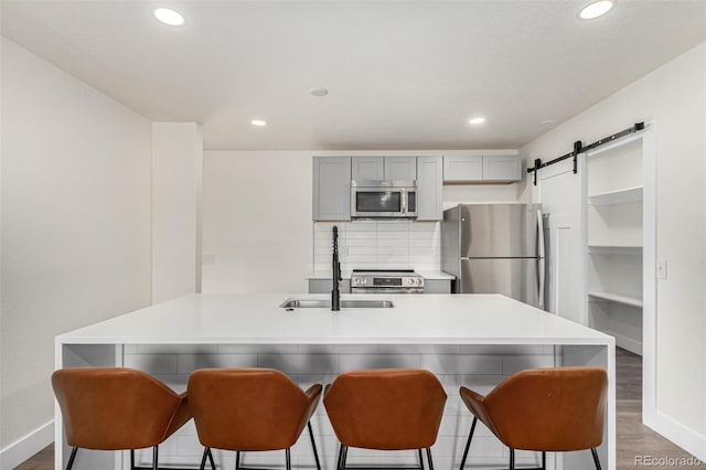 kitchen featuring dark wood-style floors, gray cabinets, stainless steel appliances, a barn door, and tasteful backsplash