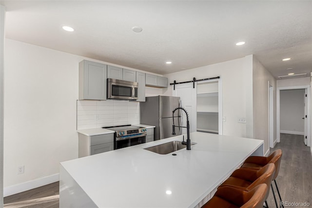 kitchen featuring a barn door, gray cabinets, appliances with stainless steel finishes, and a sink