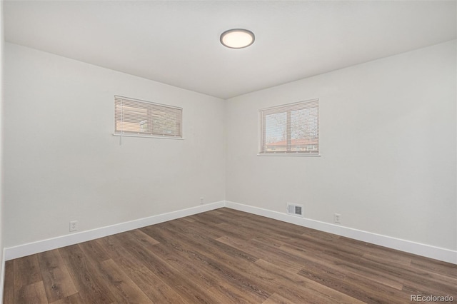 spare room featuring visible vents, dark wood-type flooring, and baseboards