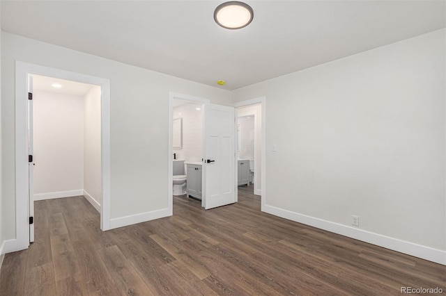 unfurnished bedroom with ensuite bath, dark wood-style floors, and baseboards