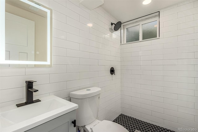 bathroom with vanity, tile walls, toilet, and tiled shower