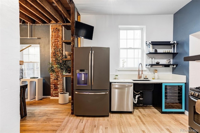 kitchen with brick wall, stainless steel appliances, beverage cooler, sink, and light hardwood / wood-style floors