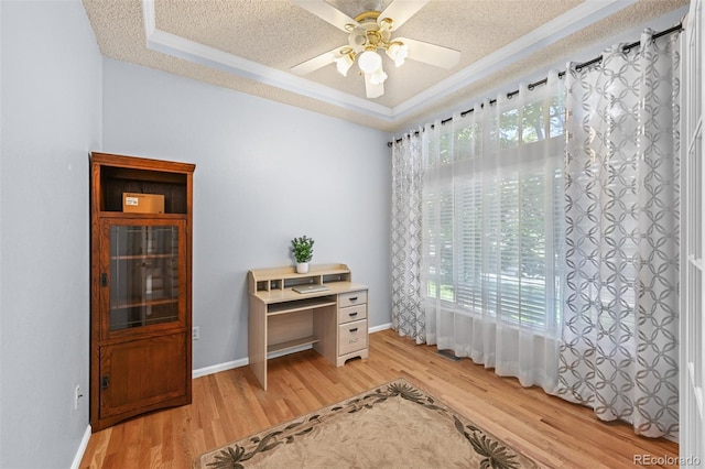office area with light wood finished floors, crown molding, ceiling fan, a tray ceiling, and baseboards