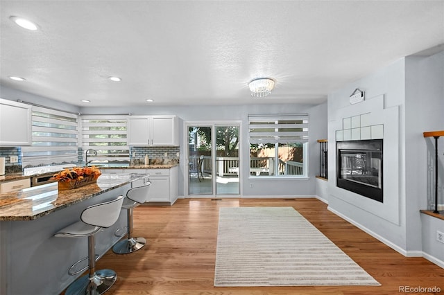 kitchen featuring a multi sided fireplace, light stone countertops, a breakfast bar, white cabinets, and recessed lighting
