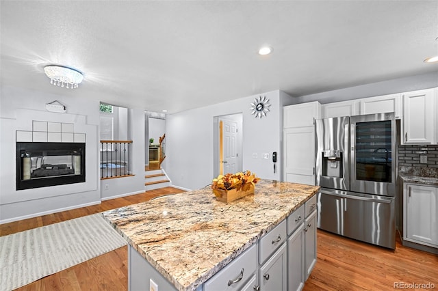 kitchen with stainless steel fridge, light wood finished floors, a center island, light stone countertops, and recessed lighting