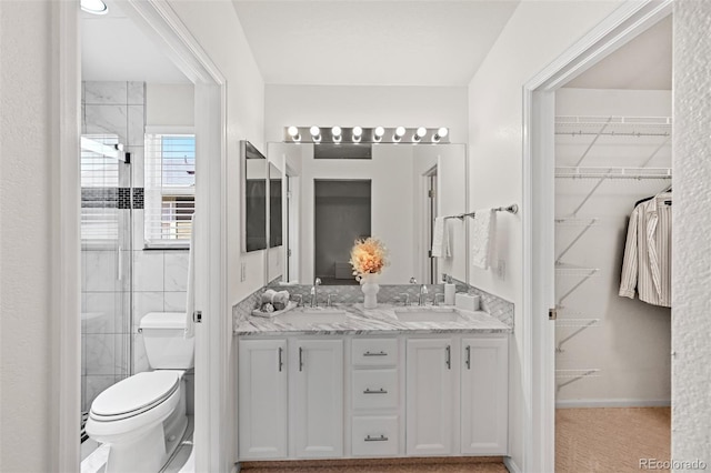 bathroom with toilet, double vanity, and a walk in closet