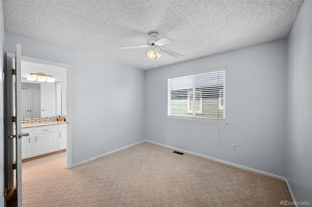 unfurnished bedroom featuring light colored carpet, a textured ceiling, baseboards, ensuite bath, and ceiling fan