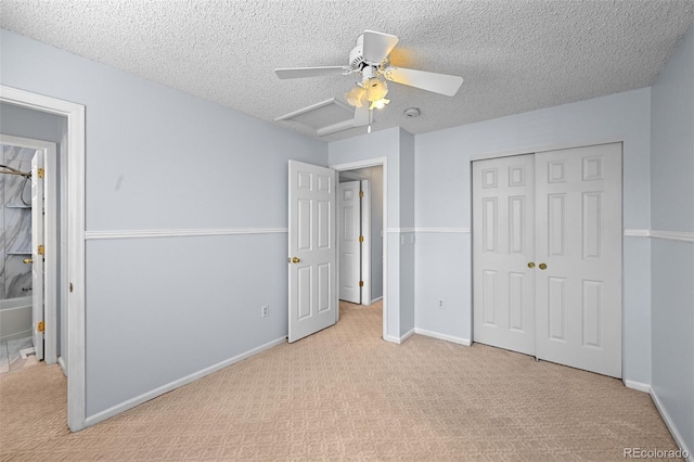 unfurnished bedroom with attic access, light colored carpet, a closet, a textured ceiling, and baseboards
