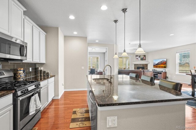 6174 Flattop St, Golden, CO 80403 - kitchen with appliances with stainless steel finishes, a sink, light wood-style flooring, decorative backsplash, and a lit fireplace
