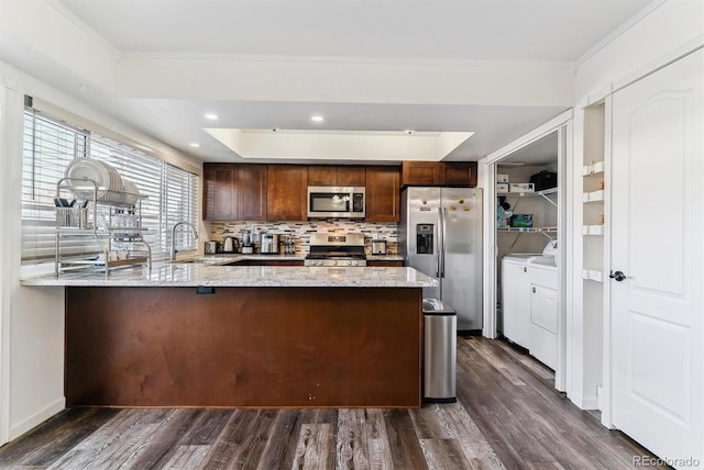 625 S Xenon Ct, Lakewood, CO 80228 - kitchen with stainless steel appliances, separate washer and dryer, a peninsula, a tray ceiling, and dark wood-style flooring