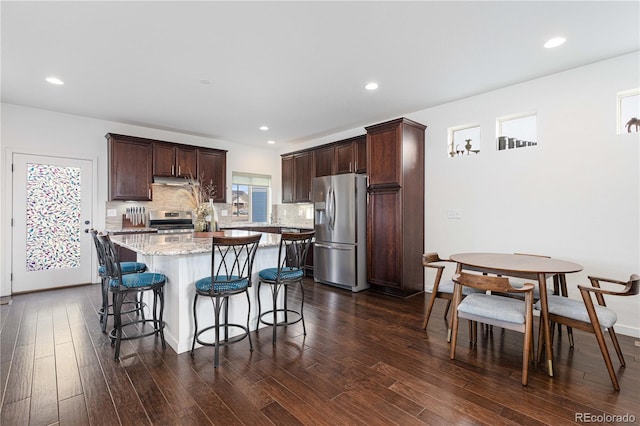 kitchen featuring dark wood-type flooring, tasteful backsplash, a center island, stainless steel appliances, and light stone countertops