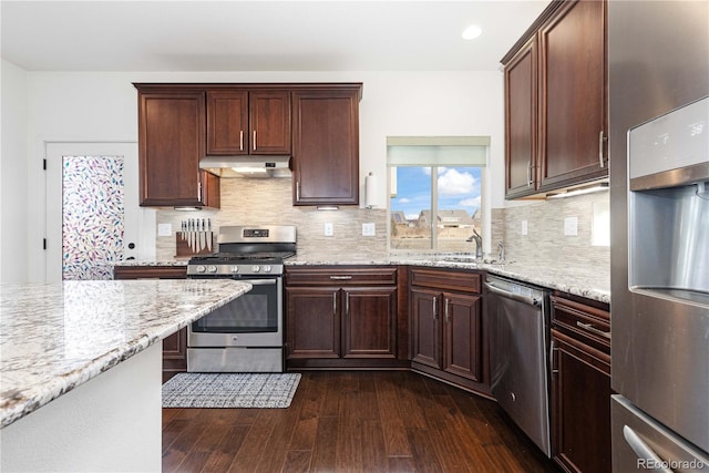 kitchen with appliances with stainless steel finishes, dark hardwood / wood-style floors, sink, backsplash, and light stone countertops