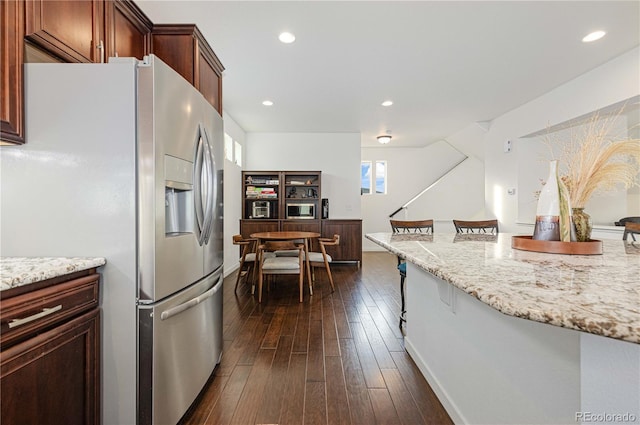 kitchen with dark hardwood / wood-style floors, light stone countertops, stainless steel fridge with ice dispenser, and a breakfast bar area