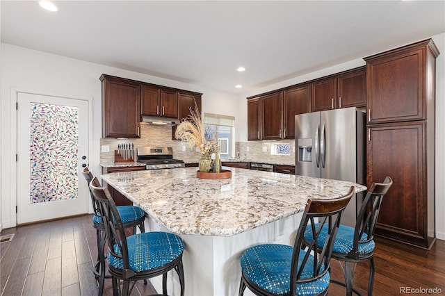 kitchen featuring appliances with stainless steel finishes, dark hardwood / wood-style flooring, a kitchen bar, and a kitchen island