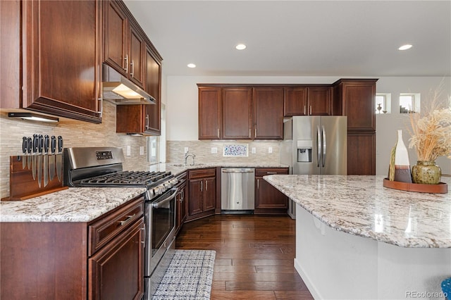 kitchen featuring appliances with stainless steel finishes, dark hardwood / wood-style floors, light stone counters, and decorative backsplash