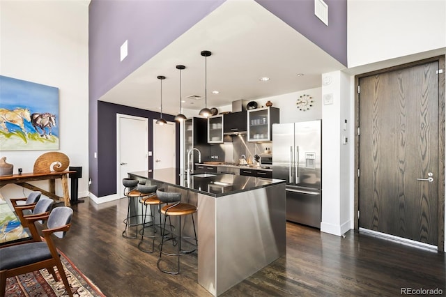 55 W 12th Ave Unit 608, Denver, CO 80204 - kitchen with stainless steel fridge, an island with sink, dark wood-style flooring, dark countertops, and glass insert cabinets