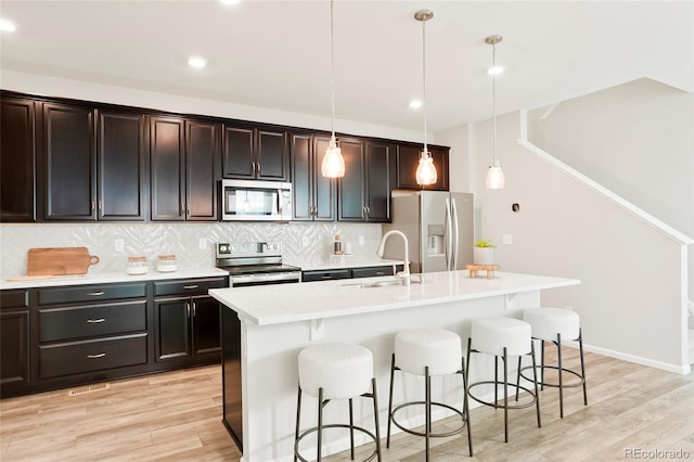 6041 N Orleans St, Aurora, CO 80019 - kitchen featuring stainless steel appliances, a breakfast bar area, light wood-style flooring, a kitchen island with sink, and light countertops