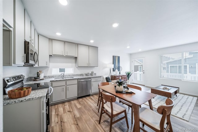 kitchen featuring light wood finished floors, gray cabinetry, recessed lighting, stainless steel appliances, and a sink