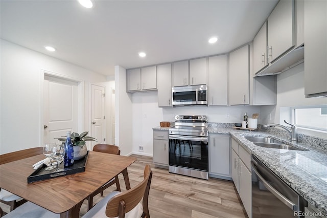 kitchen featuring light stone countertops, recessed lighting, light wood-style flooring, stainless steel appliances, and a sink