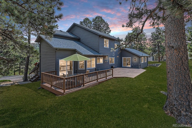 back house at dusk with a wooden deck and a lawn