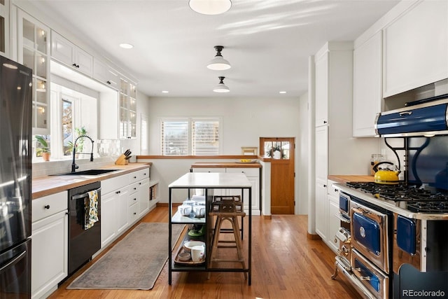 kitchen with sink, light wood-type flooring, white cabinets, a breakfast bar, and black appliances