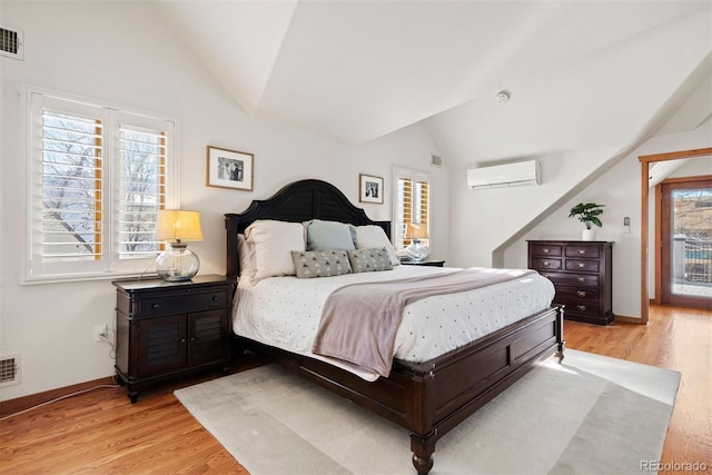 bedroom with light hardwood / wood-style floors, lofted ceiling, and a wall mounted air conditioner