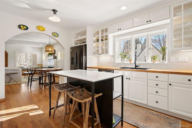 kitchen with pendant lighting, stainless steel refrigerator with ice dispenser, white cabinetry, sink, and a breakfast bar