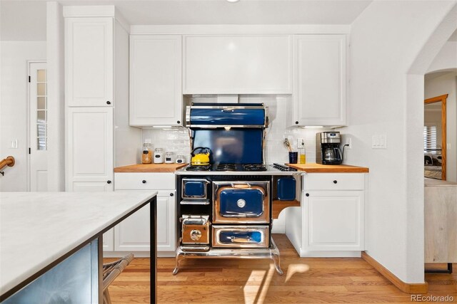 kitchen with white cabinets, wood counters, decorative backsplash, light hardwood / wood-style flooring, and stove