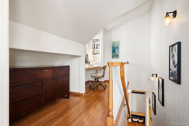 interior space with a textured ceiling, lofted ceiling, built in desk, built in features, and light wood-type flooring