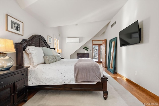 bedroom featuring an AC wall unit, light hardwood / wood-style flooring, and vaulted ceiling