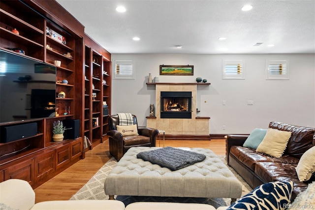 living room with light hardwood / wood-style flooring, a tile fireplace, and a textured ceiling