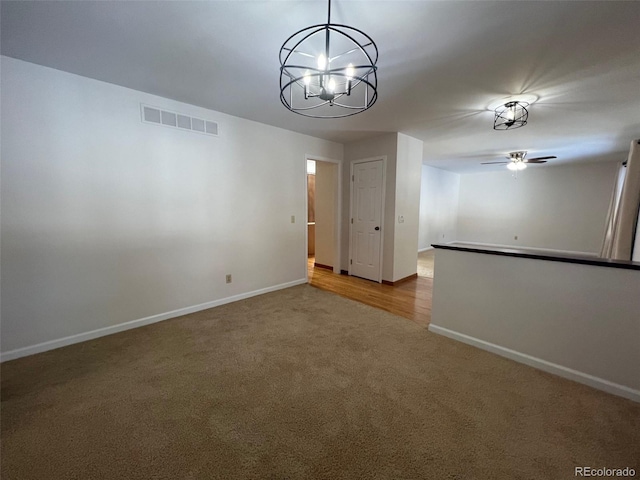 carpeted spare room with ceiling fan with notable chandelier