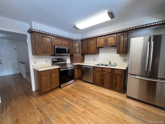 kitchen with dark brown cabinetry, sink, light wood-type flooring, and stainless steel appliances