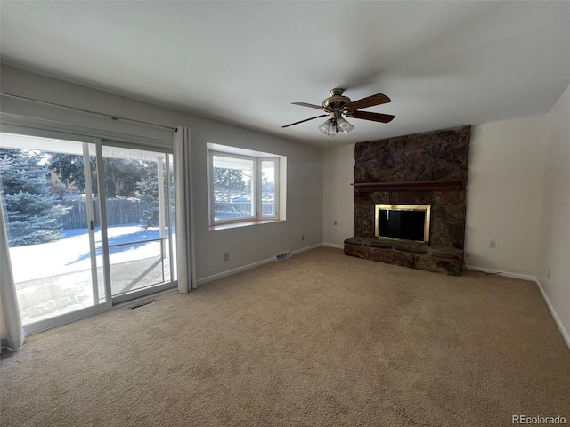 unfurnished living room featuring a wealth of natural light, a stone fireplace, light carpet, and ceiling fan